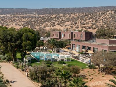 Hotel with pool and lounge chairs in a dry landscape with hills in the background