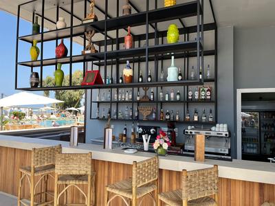 Modern outdoor bar area with wooden stools and shelves filled with bottles and glasses.