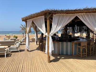 Beach bar with thatched roof, white curtains, and sun loungers by the sea