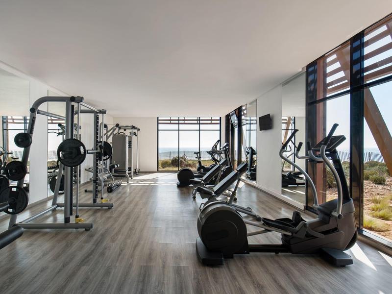 Salle de sport moderne avec équipement et grande fenêtre panoramique donnant sur la mer.