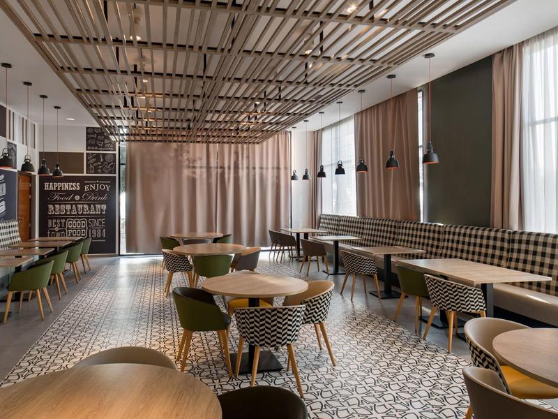 Café lumineux avec chaises en bois modernes, carrelage à motifs et grandes fenêtres avec rideaux.