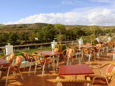 Große Terrasse mit Holzstühlen und Tischen, umgeben von Grün und Bergen im Hintergrund.