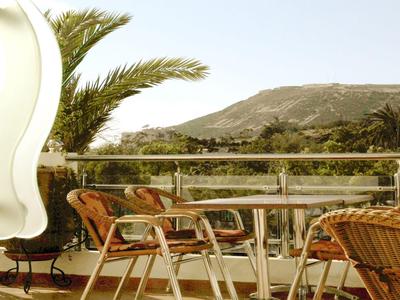 Terrazza con tavoli e sedie, palme e paesaggio montano sullo sfondo