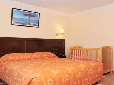 Camera d'hotel con letto matrimoniale grande, culla, comodino e quadro a parete.