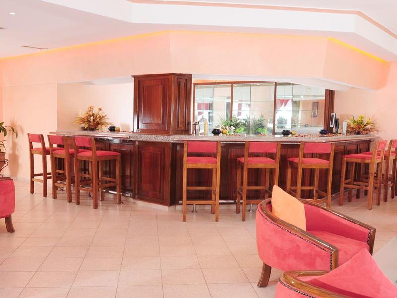 Einladender Barbereich mit Holztheke, mehreren Stühlen und roten Sesseln in hellem Raum.