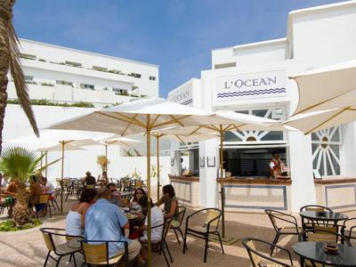 Taras kawiarni z parasolami i gośćmi przed białym budynkiem hotelu.