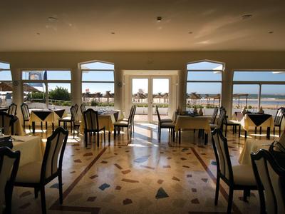 Jasna restauracja z dużymi oknami z widokiem na wodę i nakrytymi stołami.