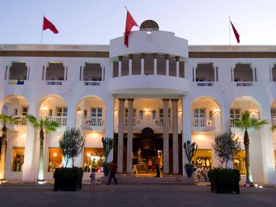 Elegancki biały budynek hotelu z kolumnami i czerwonymi flagami oświetlony o zachodzie słońca.