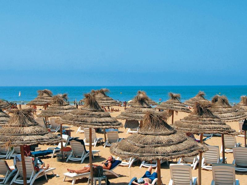 Strand mit vielen Strohdächern, blauer Himmel und ruhigem Meer im Hintergrund.