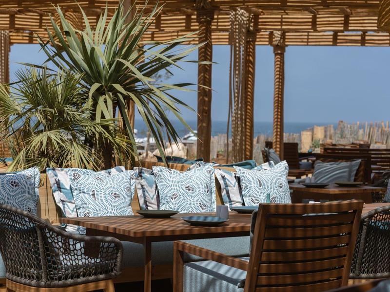 Gemütliche Sitzecke mit Holzmöbeln, Blumenmustern und Palmen auf einer Dachterrasse mit Stadtblick.