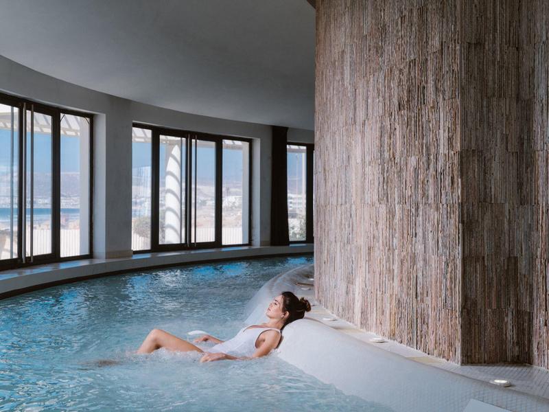 Frau entspannt im Whirlpool, umgeben von Rundfenstern mit Blick auf Himmel und Wolken.
