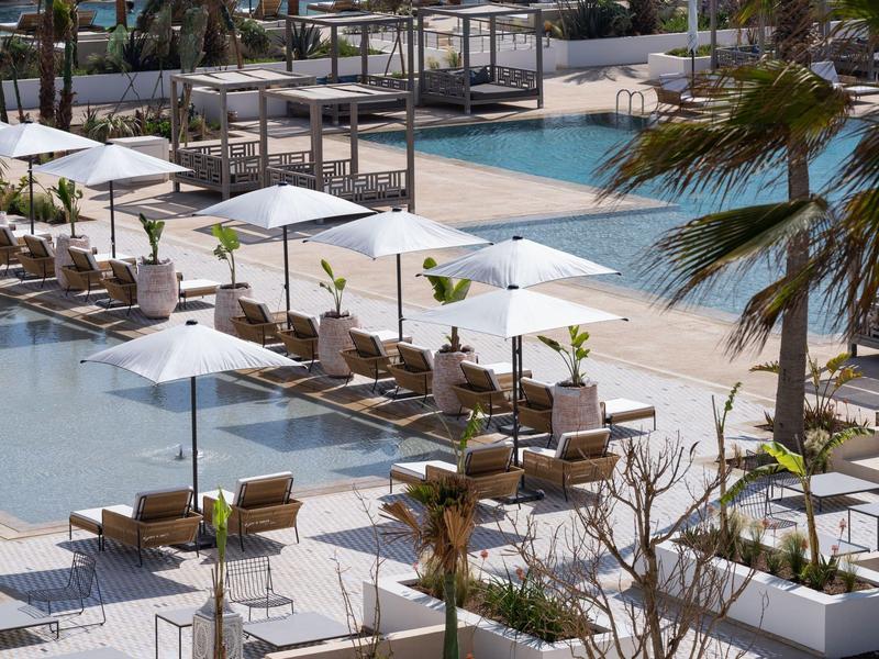 Moderner Außenpool mit Sonnenliegen und weißen Sonnenschirmen in tropischer Umgebung.