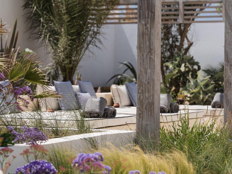 Einladender Außenbereich mit Holzpfeilern, Sitzgelegenheiten und grüner Bepflanzung bei sonnigem Wetter.