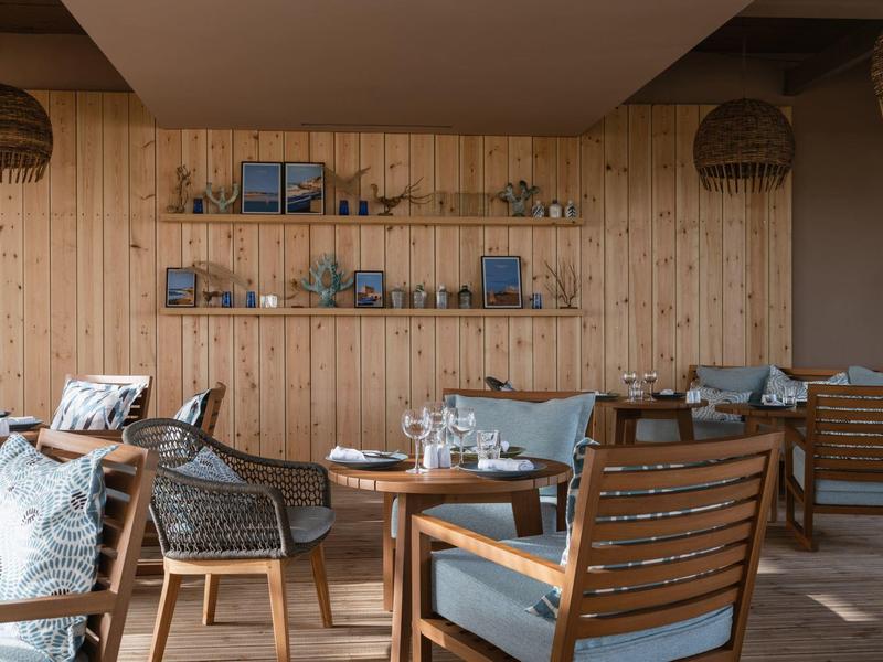 Gemütliche Lounge mit Holzwand, Sesseln mit blauen Kissen und dekorativen Regalen mit Pflanzen.