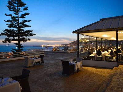 Abendliche Hotellounge mit Meerblick, gedeckten Tischen und beleuchtetem Innenbereich.