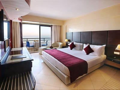 Hell eingerichtetes Hotelzimmer mit großem Bett, Balkon und Meerblick.