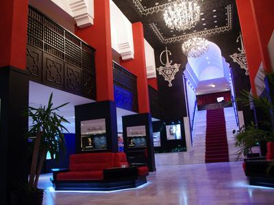 Eleganter Hotelflur mit roten und schwarzen Sitzen, weißem Marmorboden und Kronleuchtern.