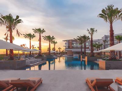 Luxusní bazén v resortu s palmami a západem slunce nad mořem.