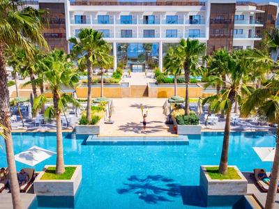 Moderní hotelový bazén s palmami a lehátky pod jasnou oblohou.