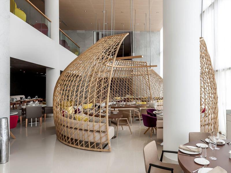 Moderner Gastraum mit hohen Decken, großen Fenstern und runder Holzstruktur als Sitzbereich.