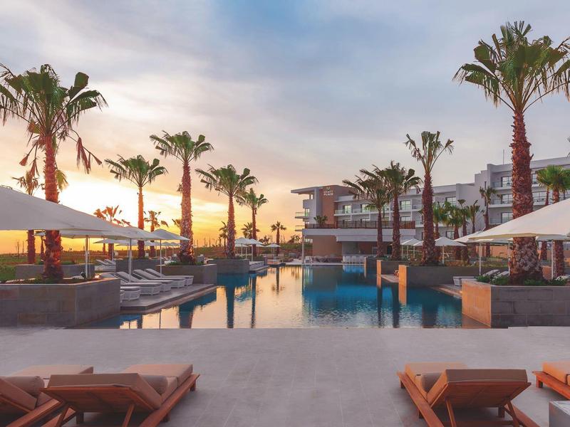 Luxuriöse Poollandschaft mit Palmen, Liegestühlen und Sonnenschirmen bei Sonnenuntergang.