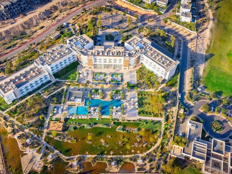 Großes Hotel mit mehreren Gebäuden, blauen Pools und grünem Golfplatz im trockenen Gelände.