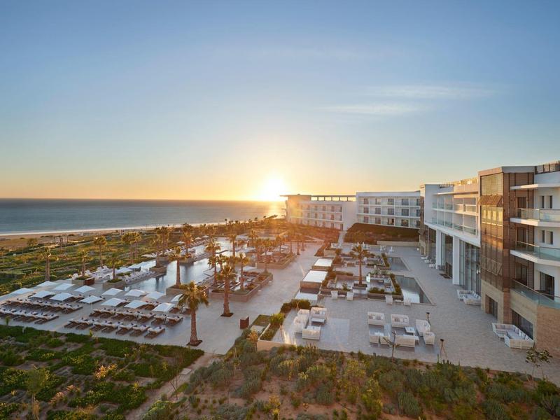 Strandhotel mit Terrasse, Liegen und Garten bei Sonnenuntergang am Meer.