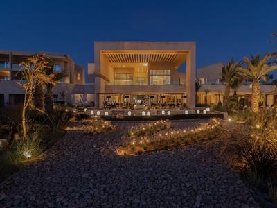 Moderní hotelová budova se osvětleným vstupem a zahradou v noci.