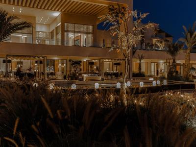 Moderní hotel s osvětlenými venkovními prostory a rostlinami v noci.