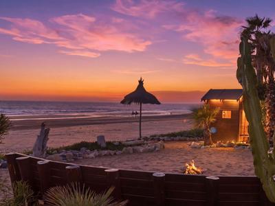 Tramonto sulla spiaggia con sabbia, ombrelloni di palma, focolare e chiosco per ospiti dell'hotel.