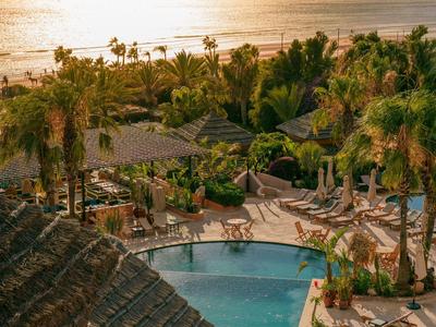 Tramonto su un resort con palme, piscina e lettini vicino al mare.
