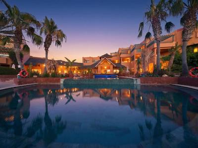 Hotel con piscina illuminata e giardini di palme al tramonto.