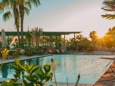 Un'area piscina tranquilla al tramonto con palme e mobili da giardino per gli ospiti.