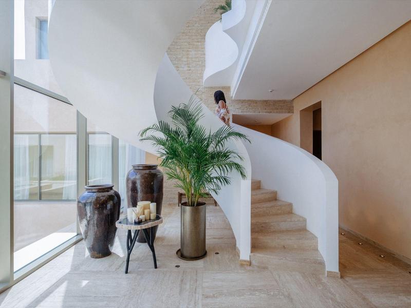 Moderner Innenraum mit geschwungener weißer Treppe, großen Glasfenstern und grüner Pflanze.