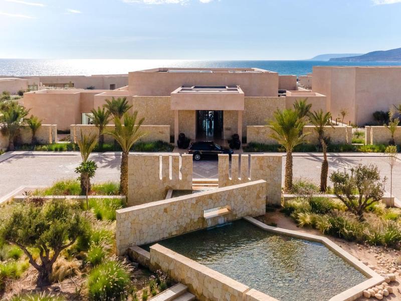 Moderner Gebäudekomplex mit Wasserbecken, Palmen und klaren Wegen in sonniger Landschaft.