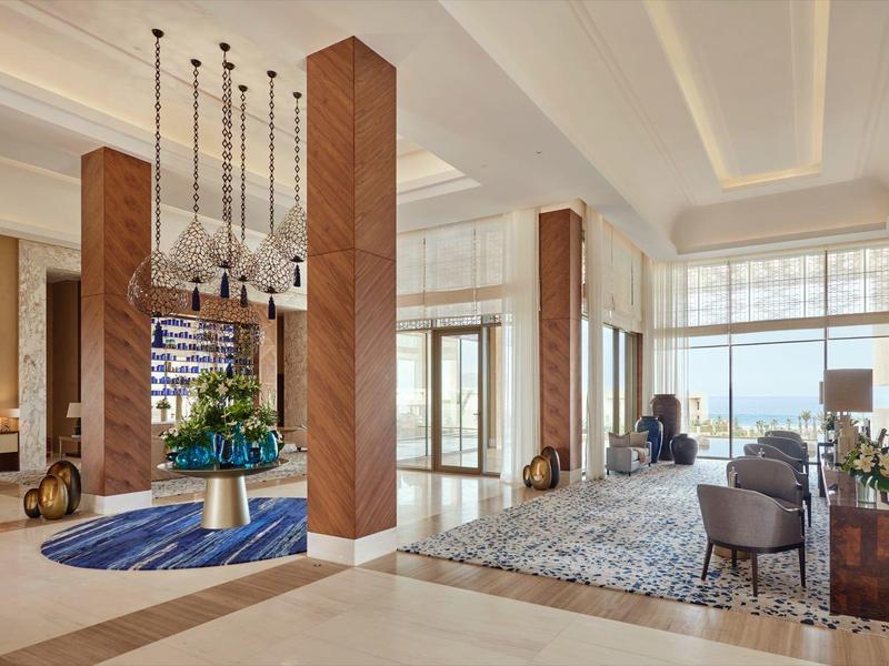 Großer, eleganter Salon mit Holzsäulen, blauen Teppichen, modernen Möbeln und großen Fenstern.