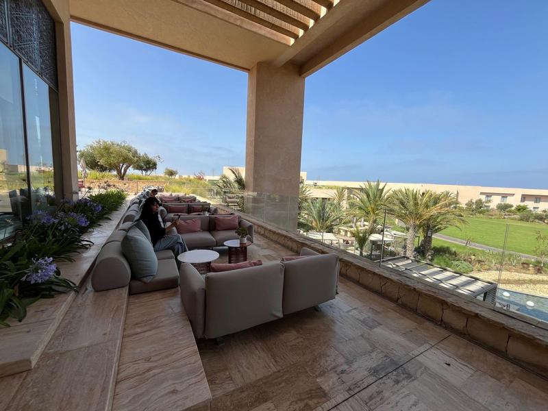 Balkon mit gemütlichen Sitzmöbeln, blauen Kissen und Blick auf Palmen und grünes Gelände.