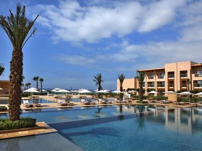 Moderner Hotelpool mit Palmen, Sonnenschirmen und mehrstöckigem Gebäude bei bewölktem Himmel