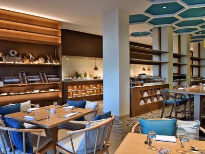 Nowoczesna restauracja hotelowa z drewnianymi meblami, niebieskimi poduszkami i dekoracyjnymi półkami.