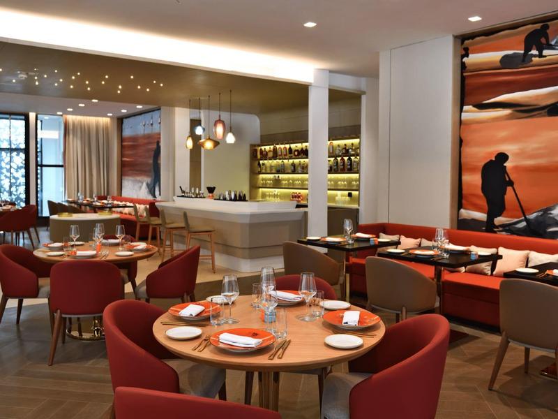 Modern hotel dining area with round tables, red chairs, and a large nature-inspired wall mural.