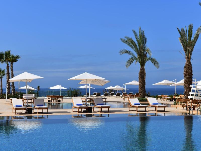 Luxury pool area with sun loungers and umbrellas under palm trees by the sea