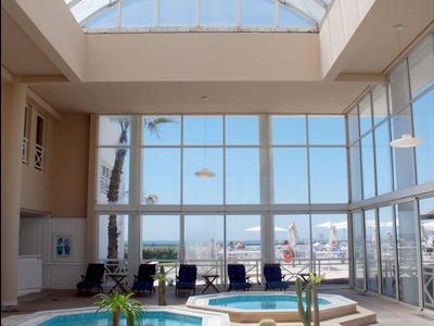 Indoor area with two hot tubs under a curved glass roof and a view of the sea.