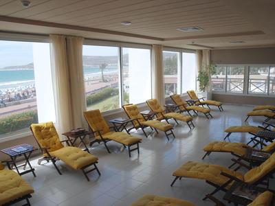 Large room with yellow lounge chairs and a view of the beach and sea through large windows.
