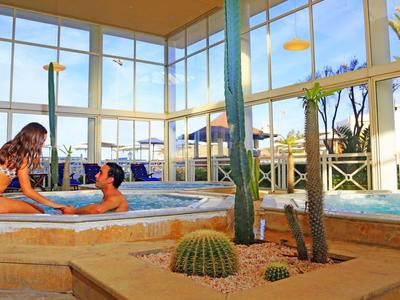 Two people relax in a hotel hot tub with large windows and plants.