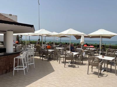 Outdoor restaurant with tables, chairs, and umbrellas overlooking the sea.
