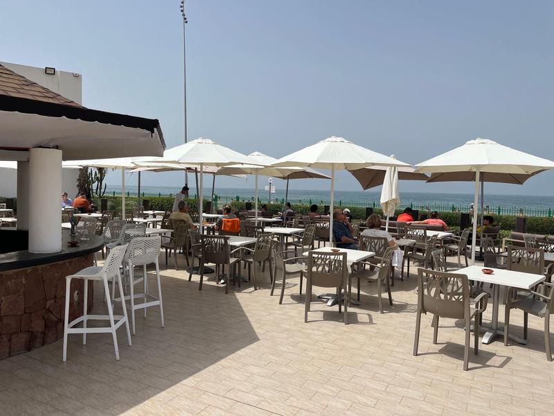 Sonnige Hotelterrasse mit Tischen, Stühlen und großen Sonnenschirmen mit Meerblick.