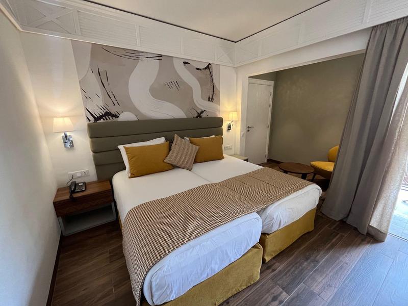 Modernes Hotelzimmer mit zwei Einzelbetten, beiger Bettdecke und abstraktem Wandbild.