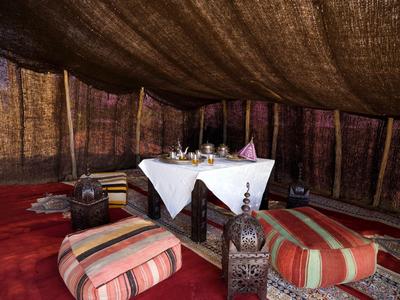 Gemütlicher Sitzbereich mit niedrigen Kissen, Teppichen und einem gedeckten Tisch in einem Zelt.