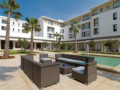 Moderner Hotelinnenhof mit Pool, Lounge-Möbeln und Palmen bei klarem Himmel.