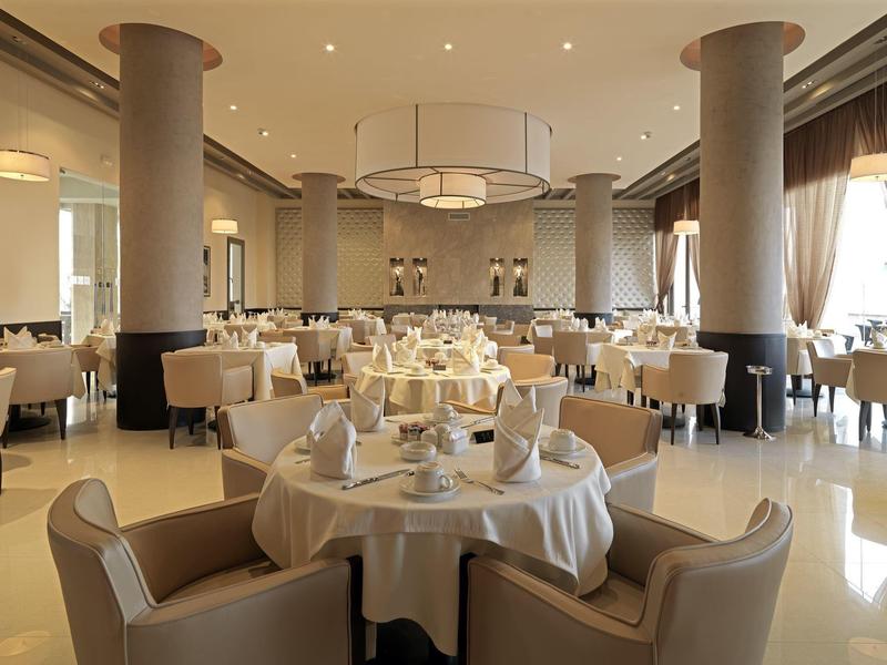 Elegancka jadalnia z okrągłymi zastawionymi stołami i beżowymi krzesłami w ciepłym oświetleniu.